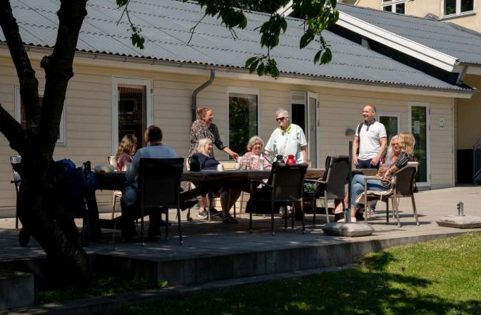 Mennesker sidder ved langt bord udenfor gult hus
